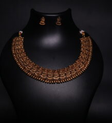 Antique gold plated temple jewellery set featuring an intricately engraved goddess motif necklace with matching jhumka earrings, displayed on a black velvet bust.