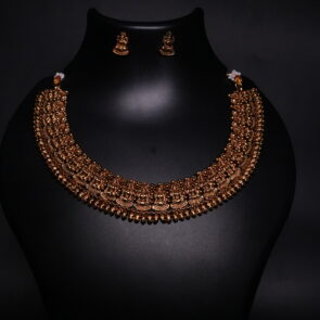 Antique gold plated temple jewellery set featuring an intricately engraved goddess motif necklace with matching jhumka earrings, displayed on a black velvet bust.
