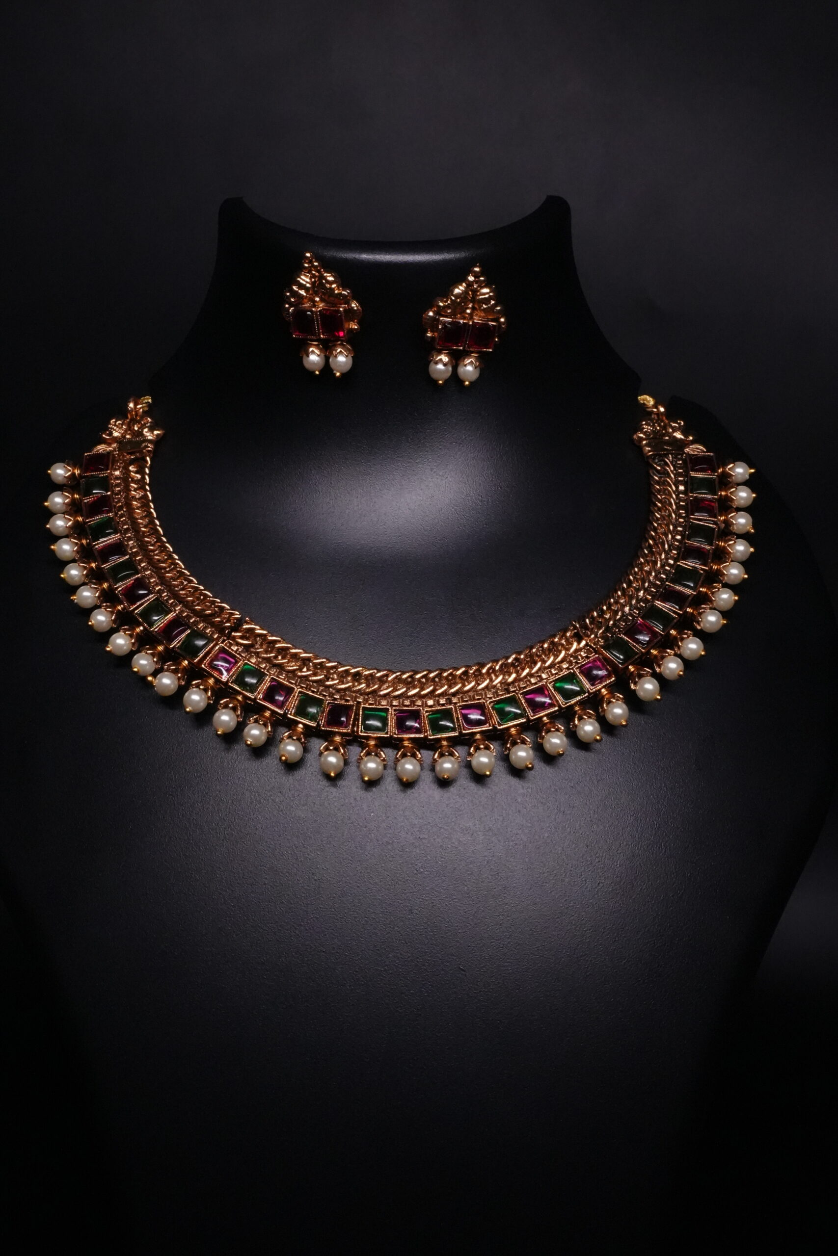 Antique gold temple kemp choker necklace and earring set with maroon and green stones and pearl drops on black display bust