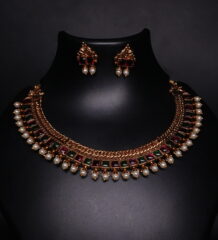 Antique gold temple kemp choker necklace and earring set with maroon and green stones and pearl drops on black display bust