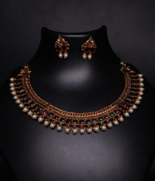 Antique gold temple kemp choker necklace and earring set with maroon and green stones and pearl drops on black display bust