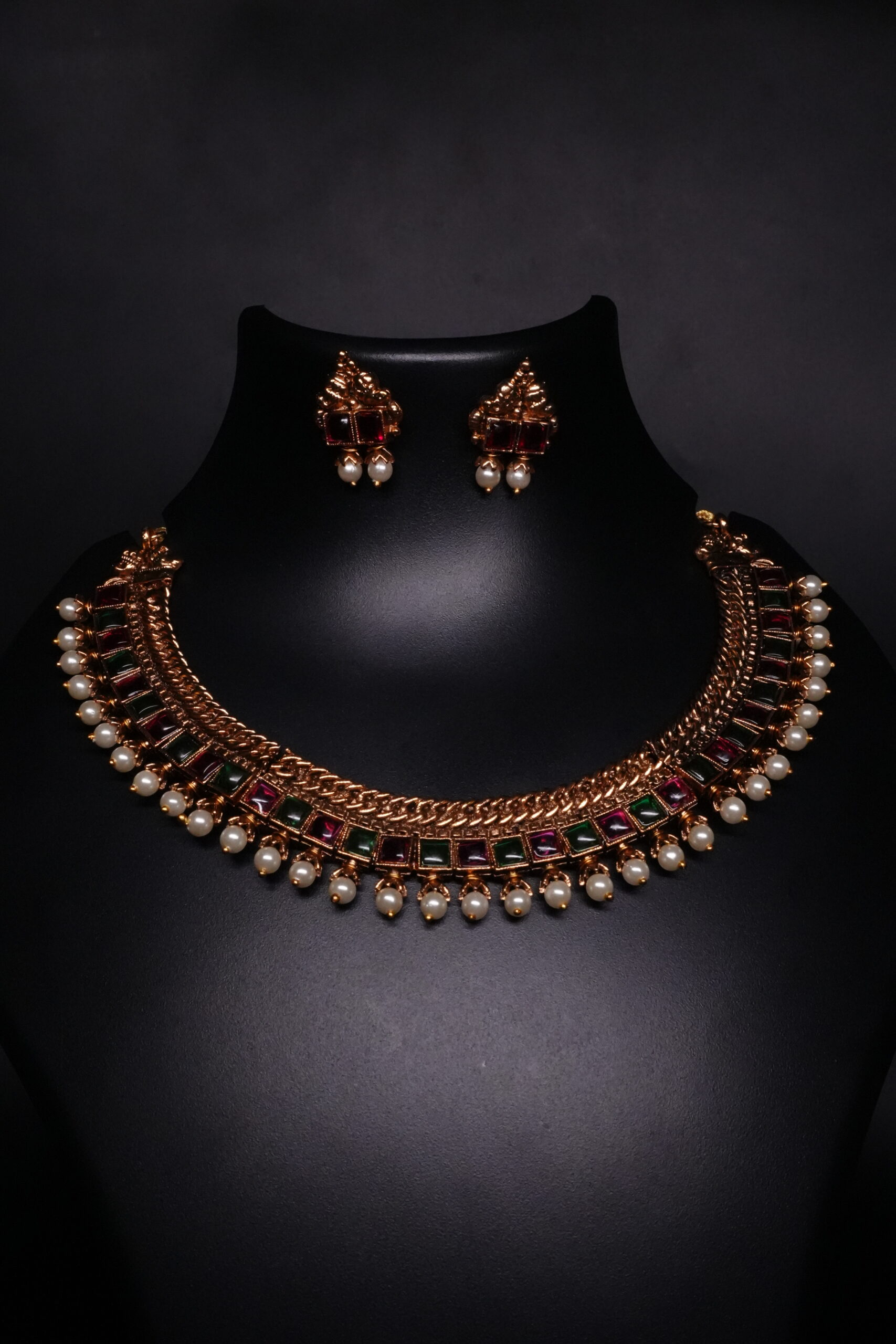 Antique gold temple kemp choker necklace and earring set with maroon and green stones and pearl drops on black display bust