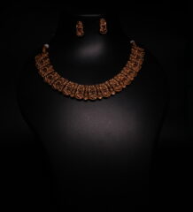Antique gold plated temple-style choker necklace and earrings set with intricate goddess motifs and red-green kemp stone accents, displayed on a black jewellery bust.