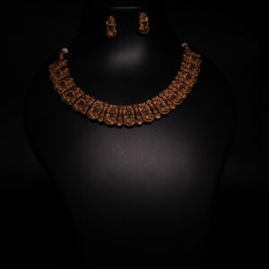 Antique gold plated temple-style choker necklace and earrings set with intricate goddess motifs and red-green kemp stone accents, displayed on a black jewellery bust.