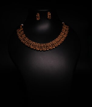 Antique gold plated temple-style choker necklace and earrings set with intricate goddess motifs and red-green kemp stone accents, displayed on a black jewellery bust.