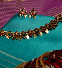 Antique gold plated necklace and earring set with red and green kemp stone heart motifs, displayed on a teal silk saree.