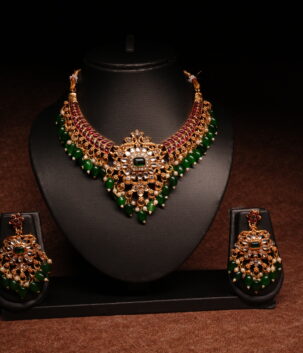 Gold plated kundan necklace set with floral motifs and deep blue beaded drops, paired with matching earrings on a black display bust