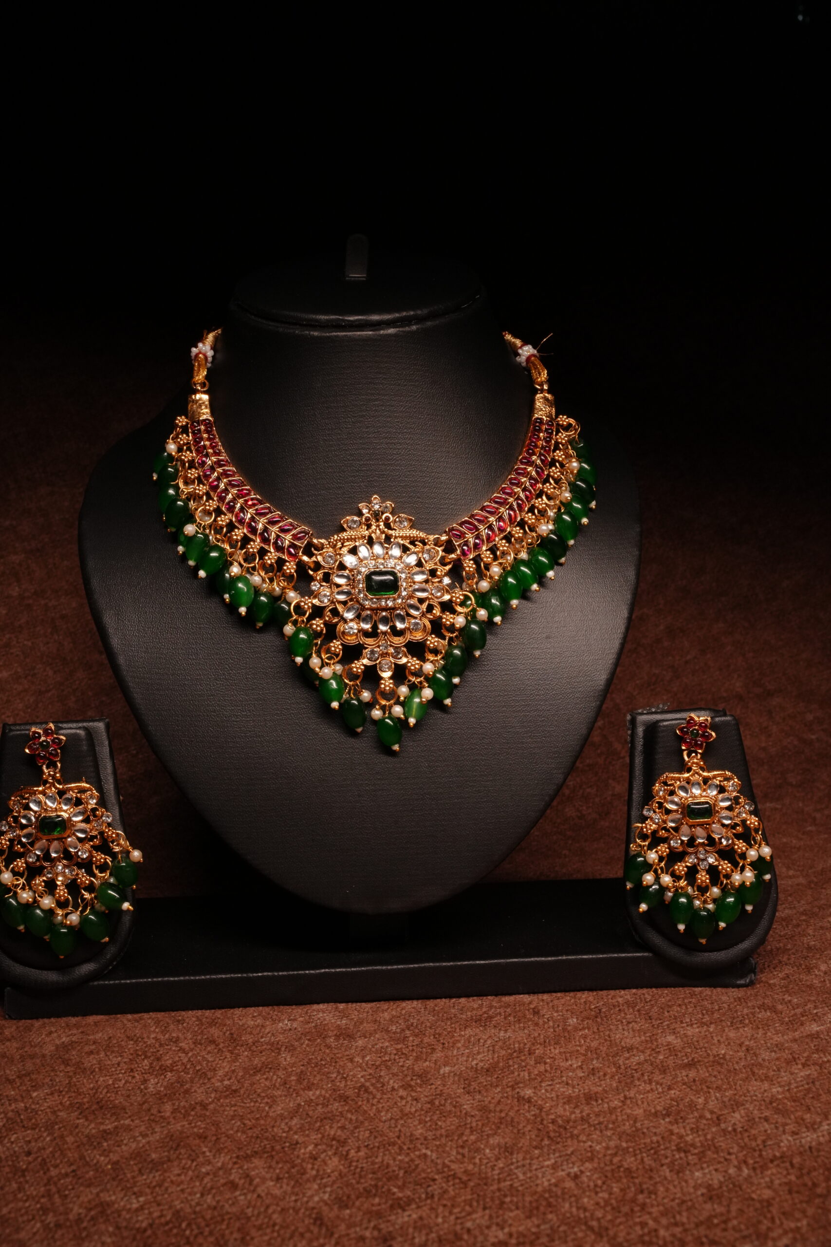Gold plated kundan necklace set with floral motifs and deep blue beaded drops, paired with matching earrings on a black display bust