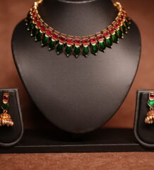 Gold plated meenakari choker necklace with green and red enamel leaf motifs, paired with matching pearl jhumka earrings on a black display bust.