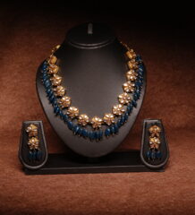 Gold plated meenakari choker necklace with green and red enamel leaf motifs, paired with matching pearl jhumka earrings on a black display bust.