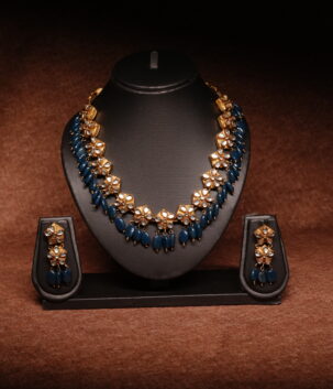 Gold plated meenakari choker necklace with green and red enamel leaf motifs, paired with matching pearl jhumka earrings on a black display bust.