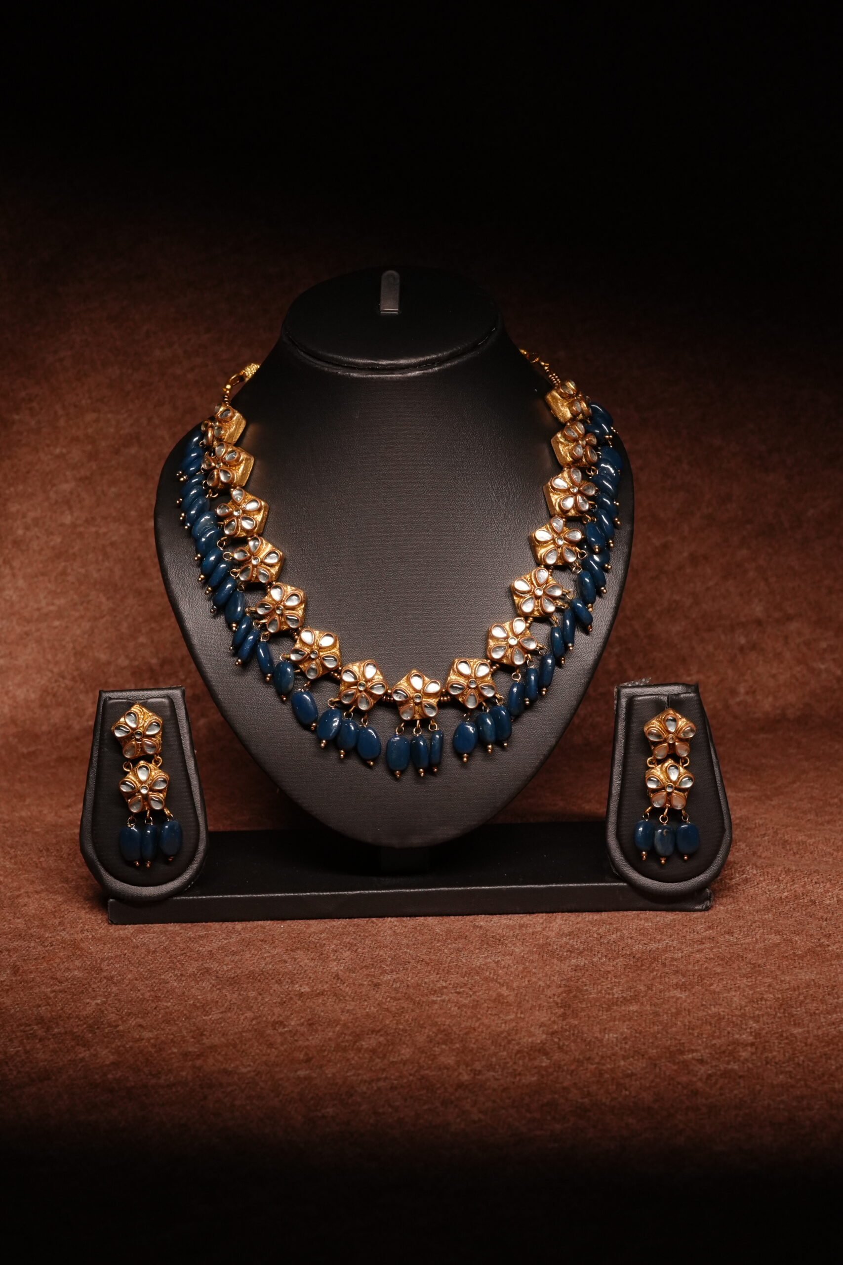 Gold plated meenakari choker necklace with green and red enamel leaf motifs, paired with matching pearl jhumka earrings on a black display bust.