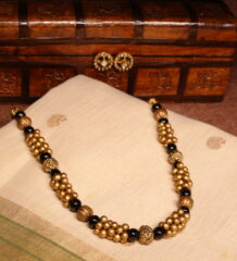 Antique gold plated necklace with clustered gold beads and black bead accents, paired with matching black-and-gold stud earrings, displayed on a carved wooden box and traditional cream saree.