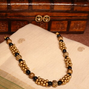 Antique gold plated necklace with clustered gold beads and black bead accents, paired with matching black-and-gold stud earrings, displayed on a carved wooden box and traditional cream saree.
