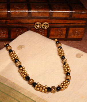 Antique gold plated necklace with clustered gold beads and black bead accents, paired with matching black-and-gold stud earrings, displayed on a carved wooden box and traditional cream saree.