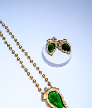Gold plated antique-finish beaded necklace and stud earring set featuring a green enamelled paisley design bordered with sparkling white crystal stones, displayed on a white background.