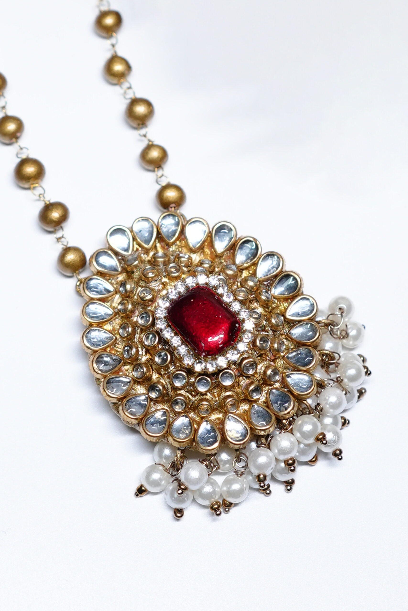Close-up of kundan pendant necklace set showing red centre stone, gold beads, and pearl drop detailing.