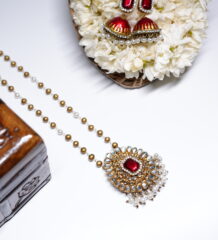 Gold plated Kundan pendant necklace with a red centre stone and matching pearl-drop jhumka earrings, displayed on a bed of white jasmine flowers.