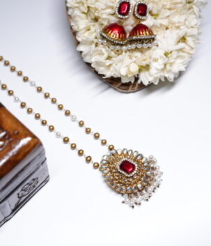 Gold plated Kundan pendant necklace with a red centre stone and matching pearl-drop jhumka earrings, displayed on a bed of white jasmine flowers.