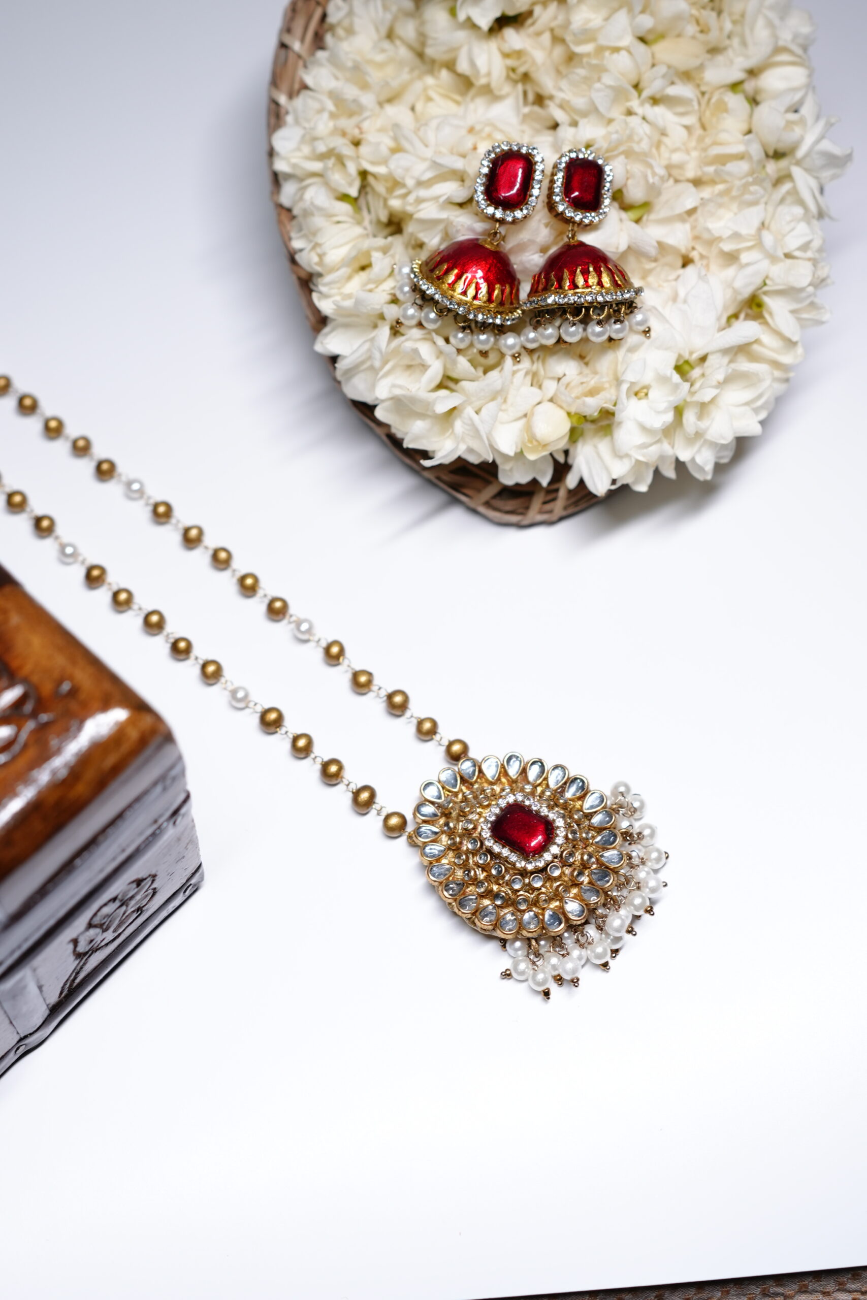 Gold plated Kundan pendant necklace with a red centre stone and matching pearl-drop jhumka earrings, displayed on a bed of white jasmine flowers.