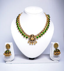 Gold plated temple-style necklace set with green kundan stones and a Goddess Lakshmi pendant, paired with matching jhumka earrings.