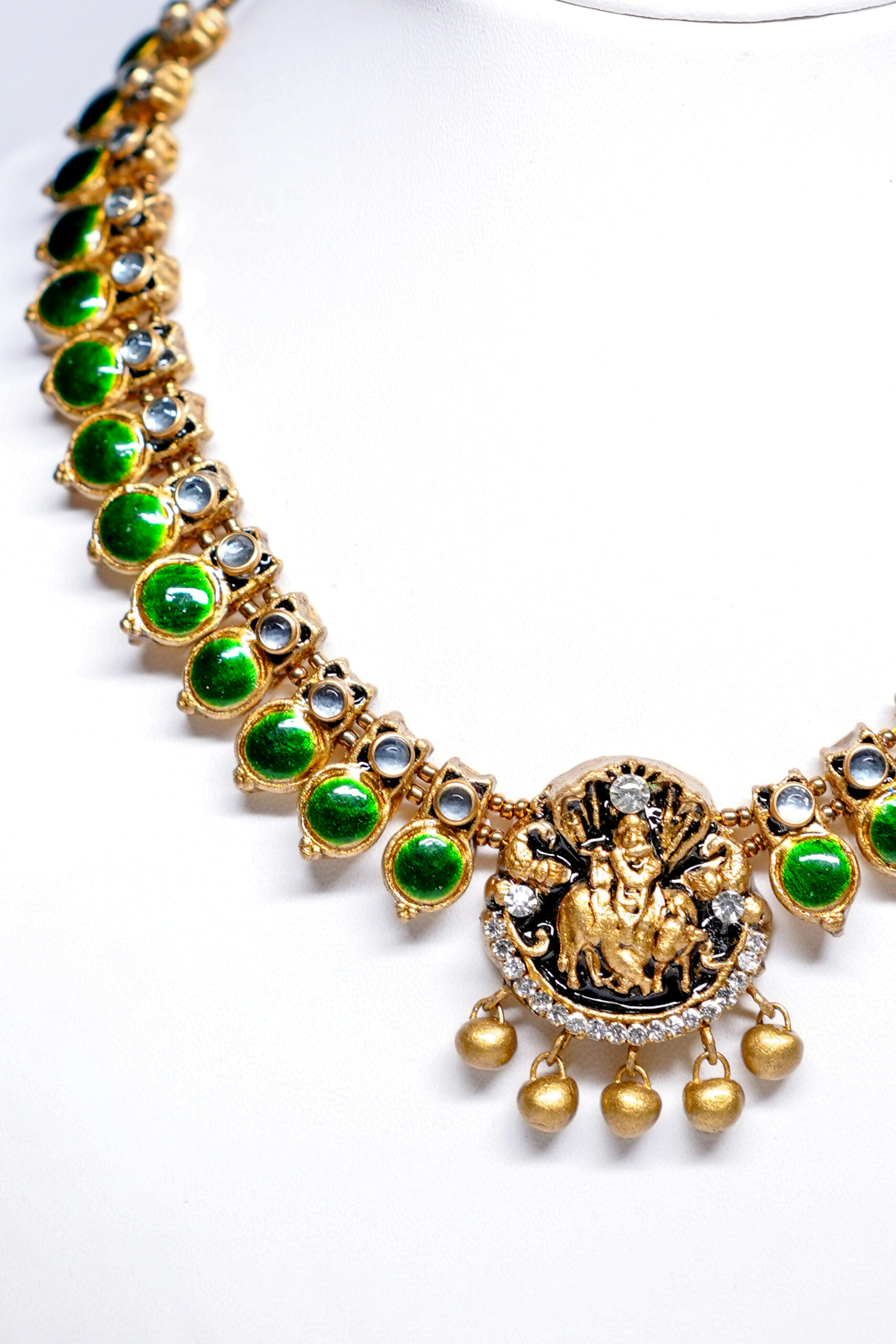 Gold plated temple necklace set with green kundan stones and Goddess Lakshmi pendant displayed with matching jhumka earrings.