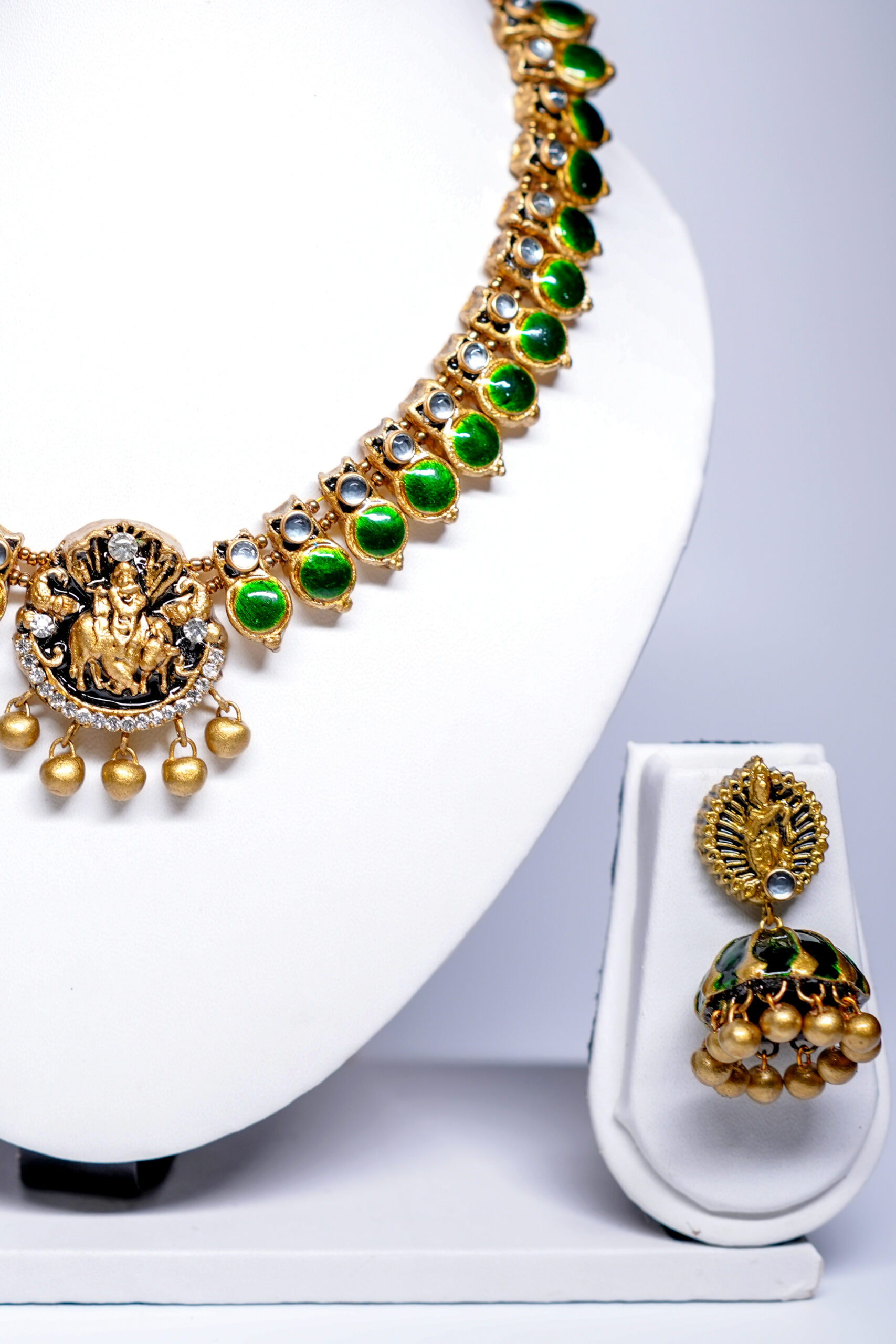Close-up of gold plated temple necklace set showing green kundan stonework, Lakshmi pendant detailing, and gold bead jhumka earrings.