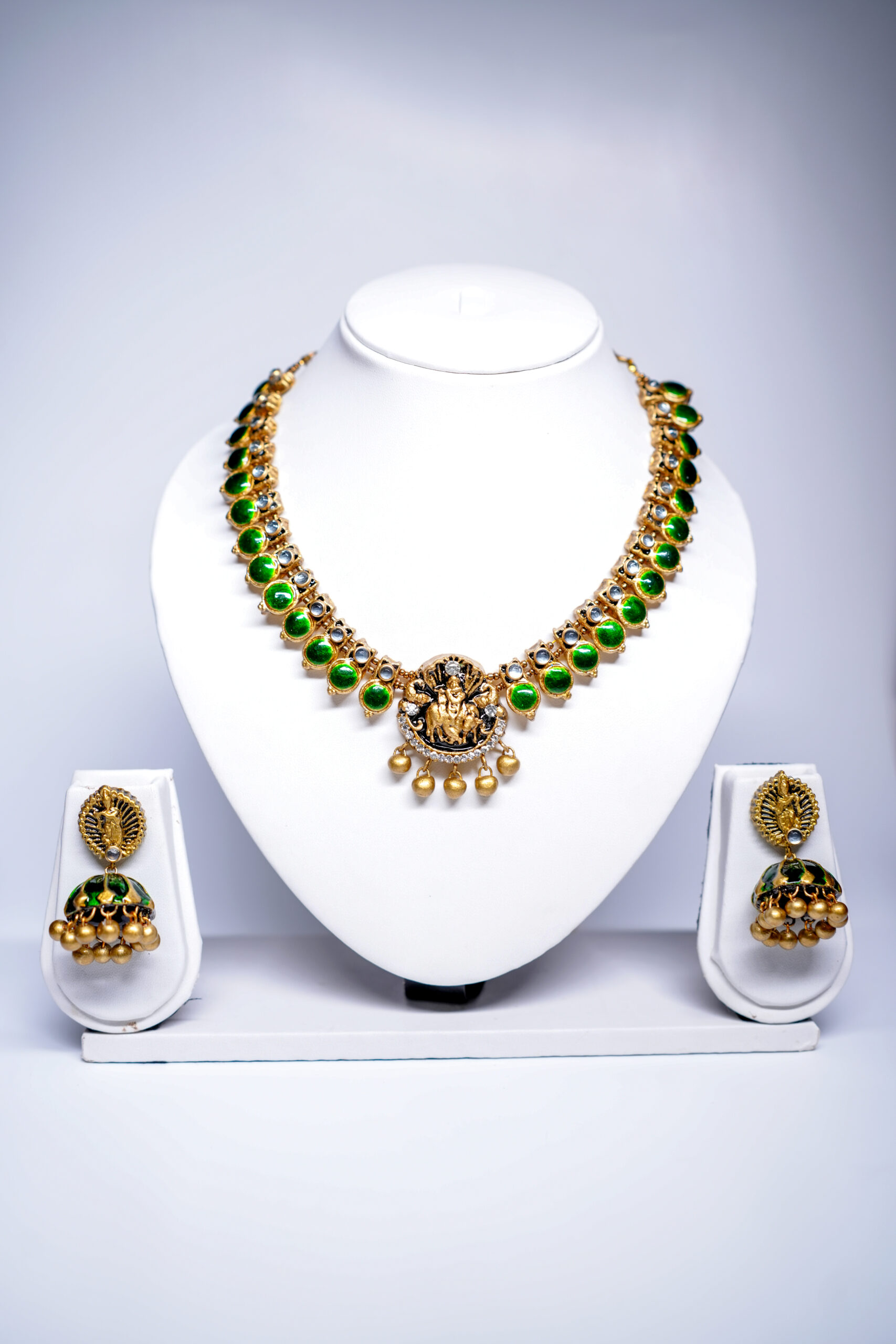 Gold plated temple-style necklace set with green kundan stones and a Goddess Lakshmi pendant, paired with matching jhumka earrings.