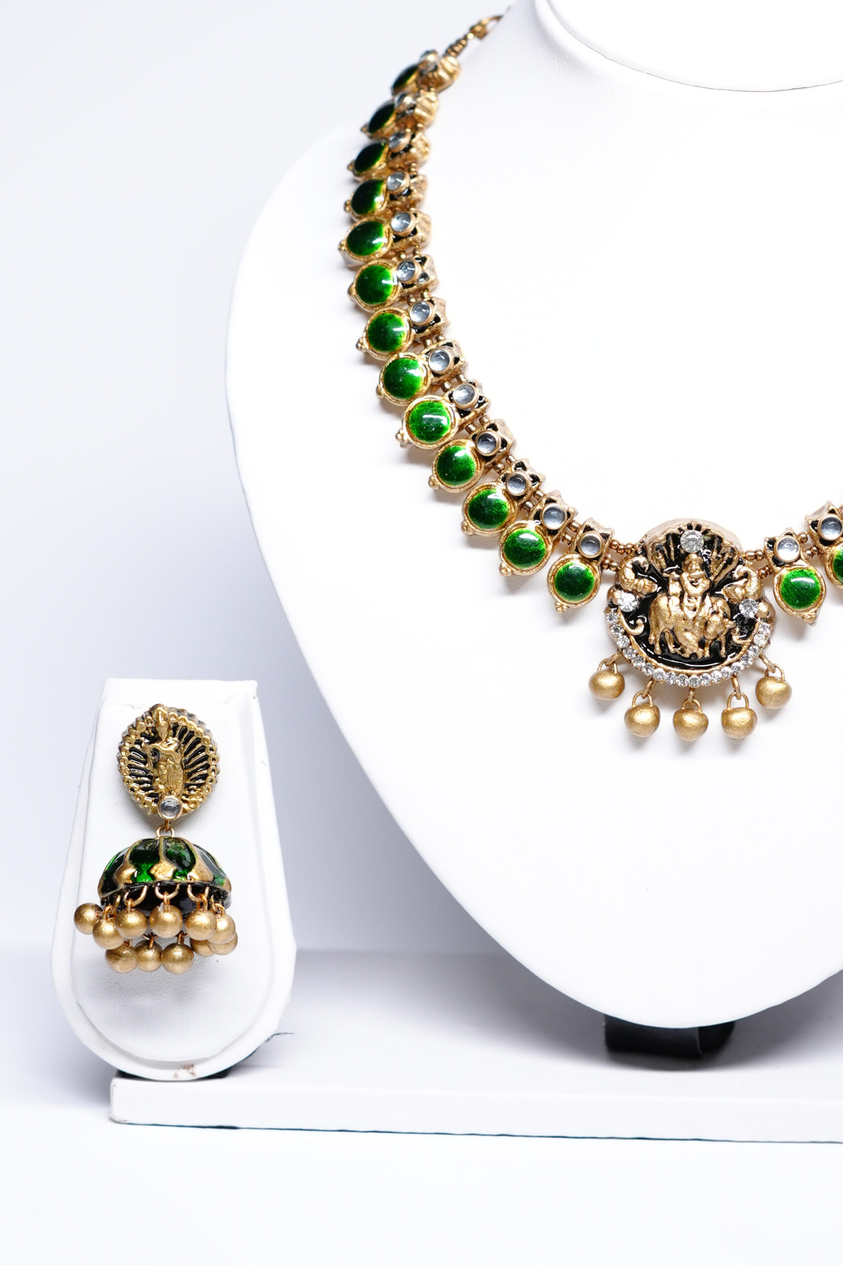 Close-up of gold plated kundan necklace set showing green stone detailing and matching jhumka earrings.