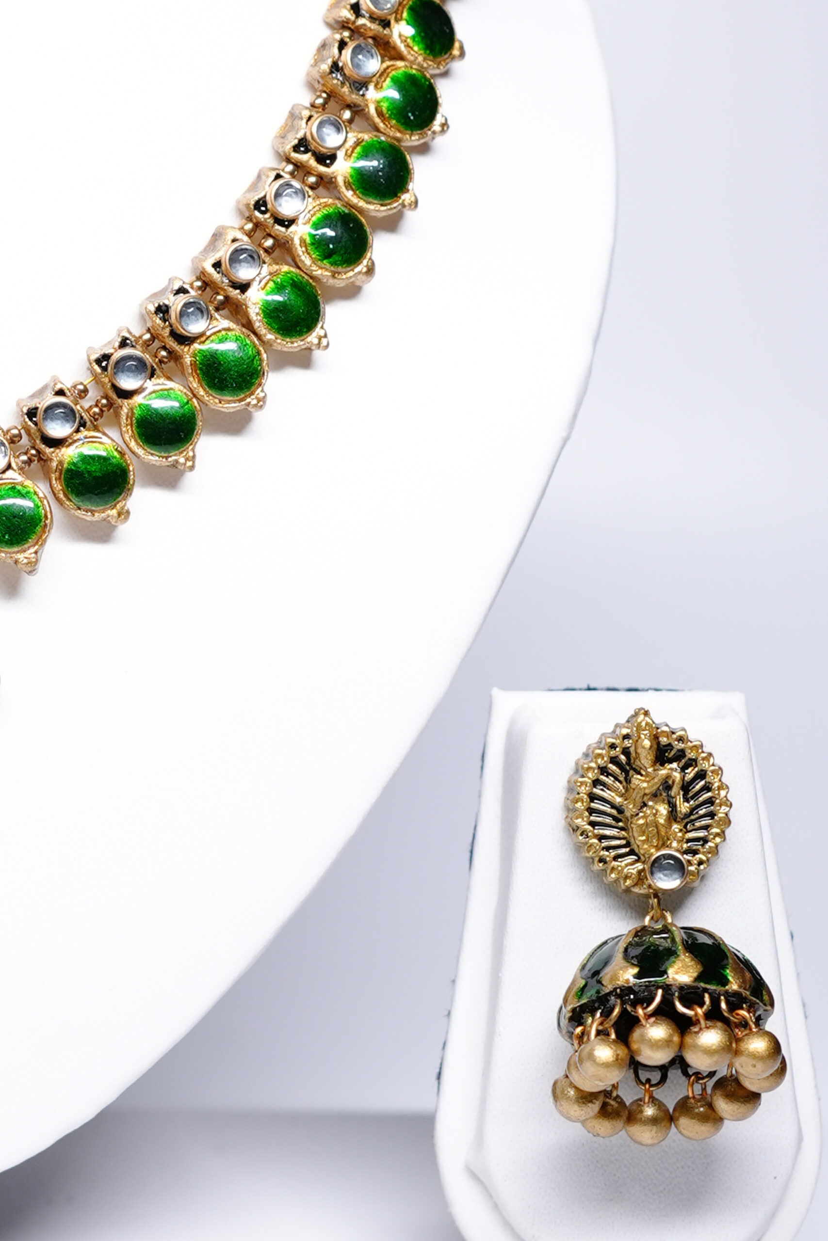 Close-up of gold plated kundan necklace set showing green stone detailing and matching jhumka earrings.
