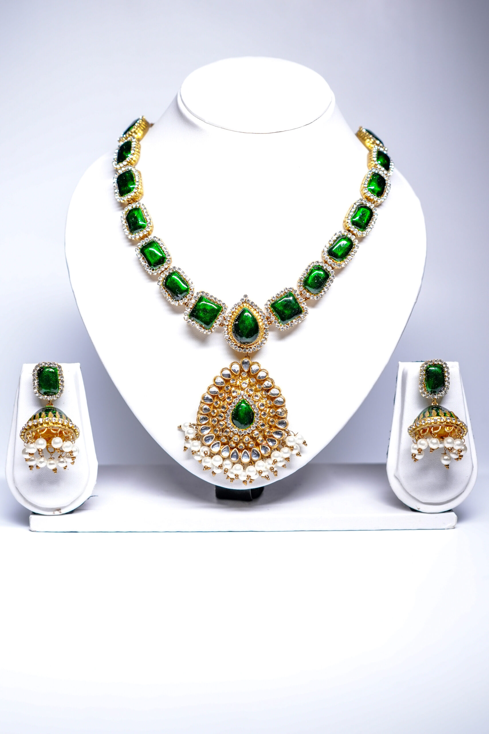 Gold plated bridal necklace set with emerald-green kundan stones and pearl-fringed pendant, paired with matching jhumka earrings.