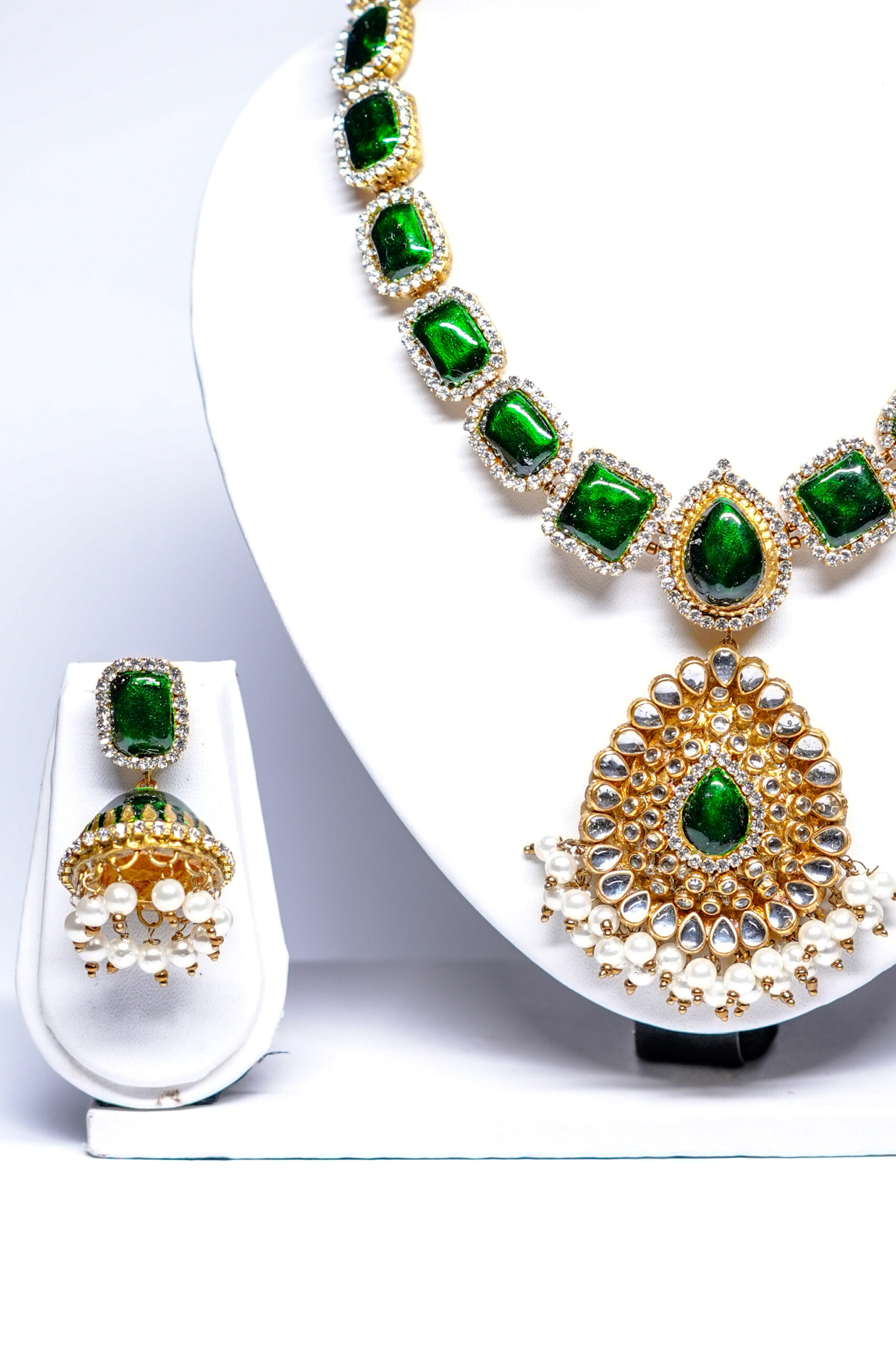 Gold plated kundan necklace set with green stones and pearl-fringed pendant on a white display bust.