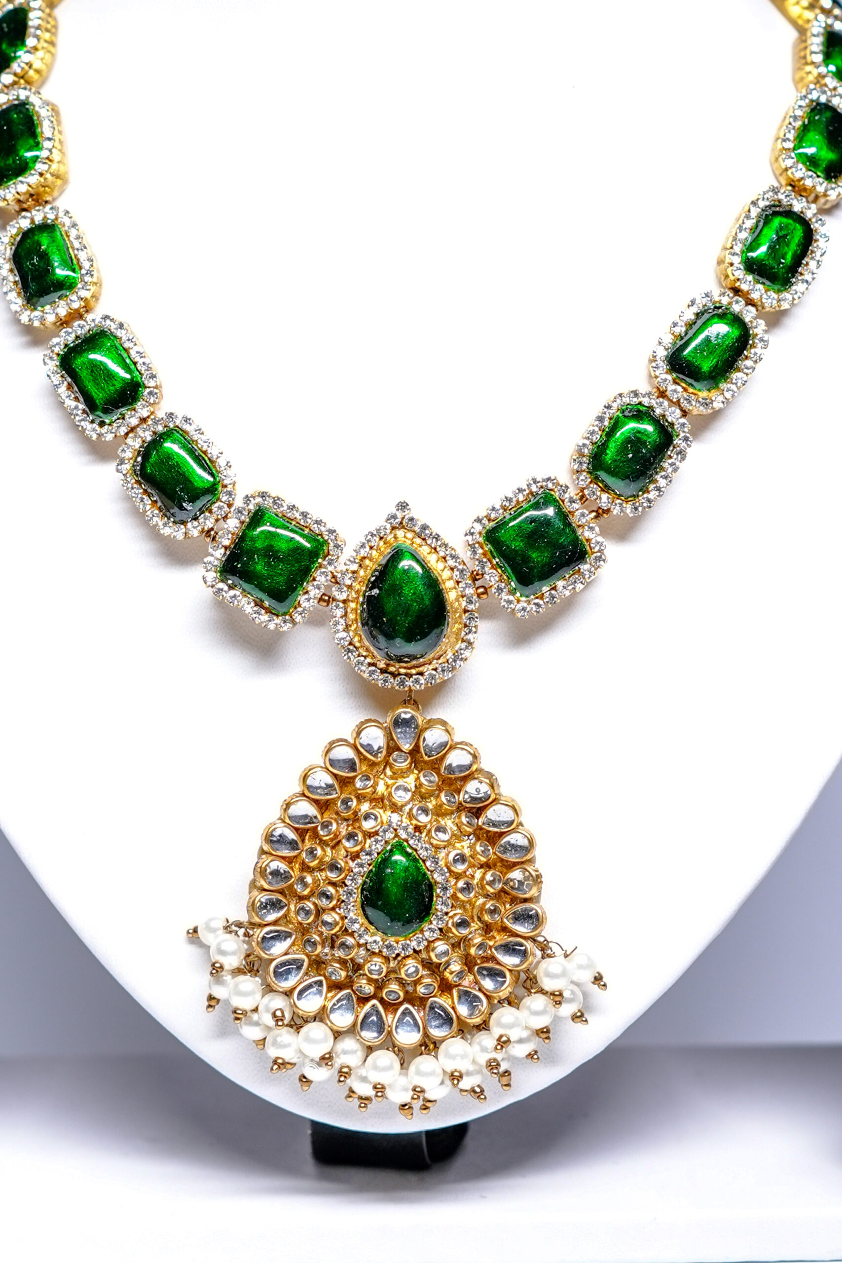 Close-up of gold plated kundan necklace set showing green stone detailing and matching pearl jhumka earrings.