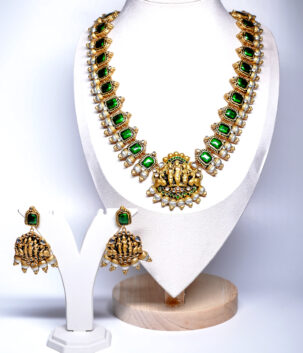 Gold plated temple jewellery set with green stone necklace, Goddess Lakshmi pendant, and matching jhumka earrings displayed on a mannequin.
