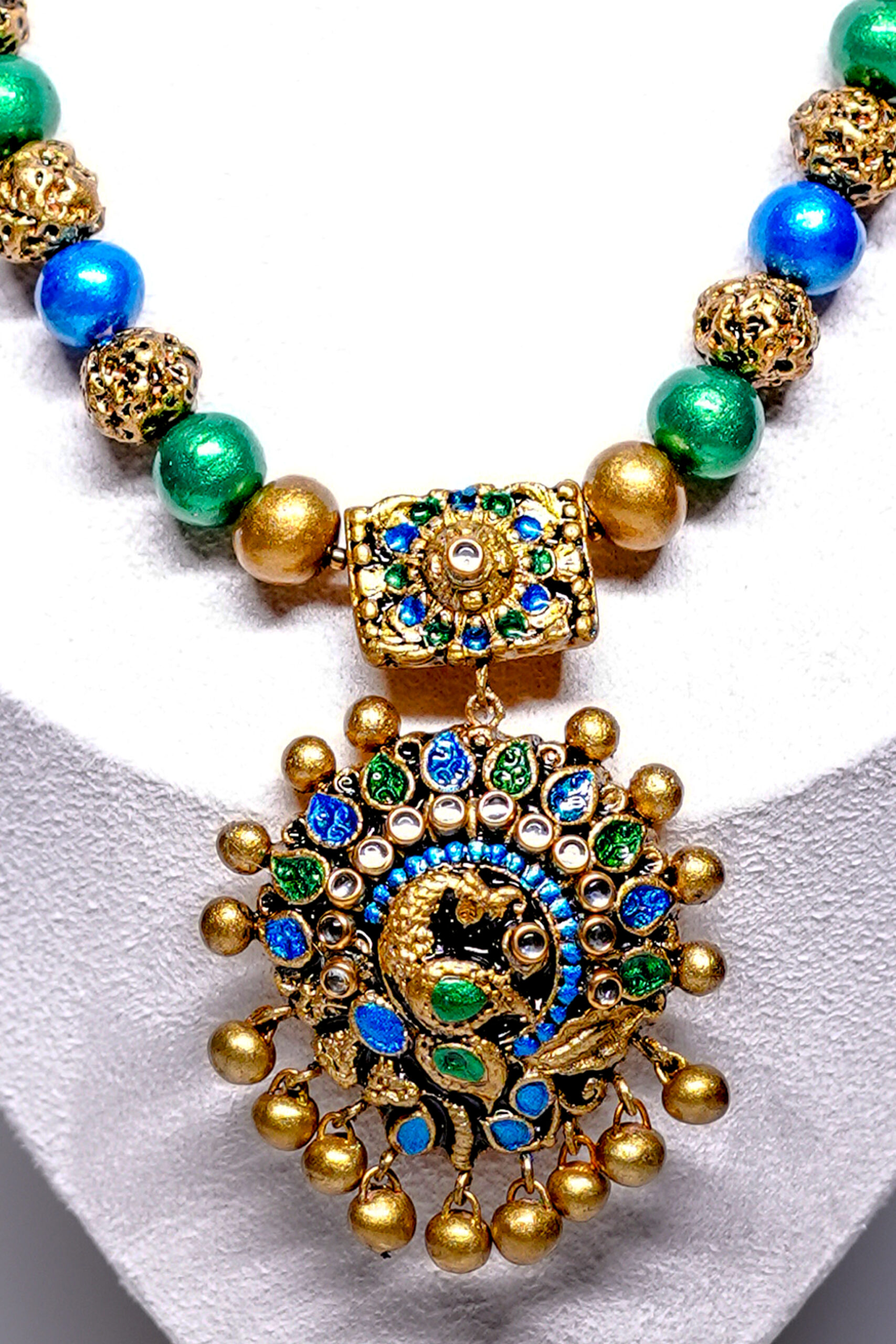 Close-up of meenakari peacock pendant with blue and green enamel work and matching gold beaded jhumka earrings.