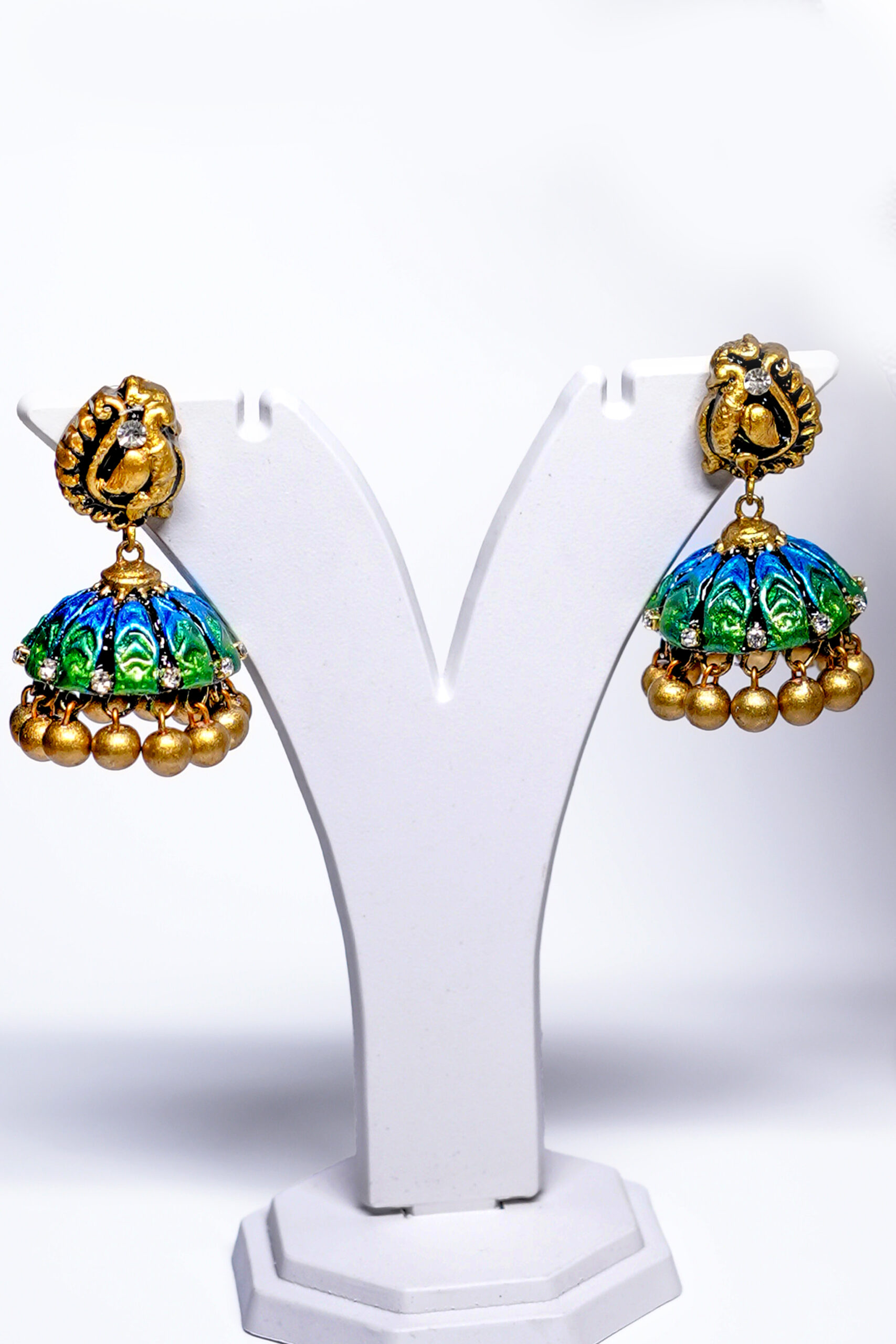 Close-up of meenakari peacock pendant with blue and green enamel work and matching gold beaded jhumka earrings.