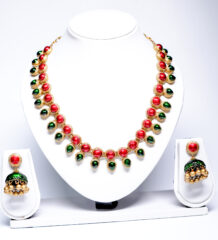 Gold plated necklace with alternating red and green kemp stones and matching jhumka earrings displayed on a white jewellery bust.