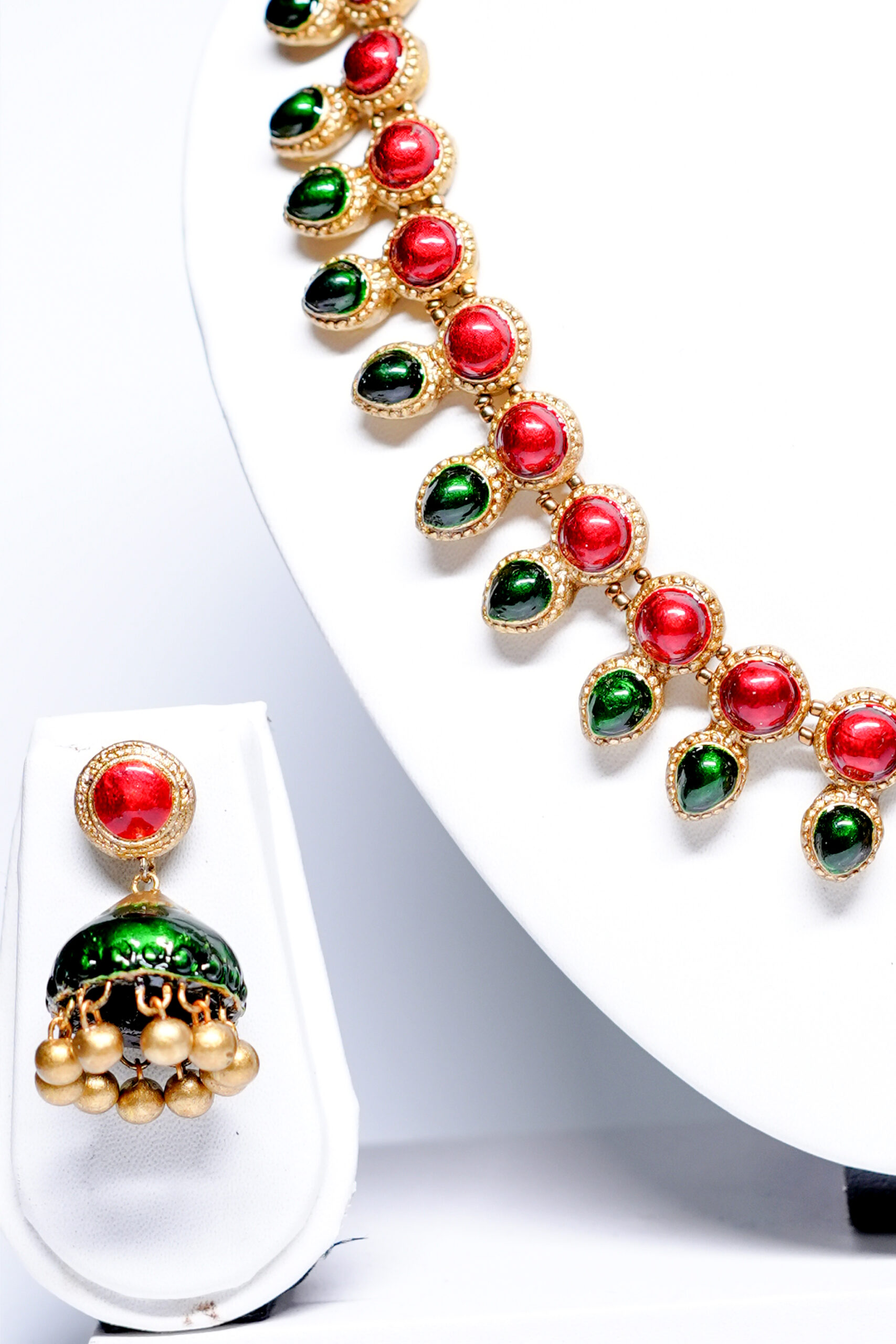 Close-up of gold plated kemp necklace showing ruby-red and emerald-green stone detailing with matching jhumka earrings.