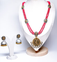 A pink beaded double-strand necklace with an antique gold temple-style kundan pendant, paired with matching silver-and-gold jhumka earrings, displayed on a white jewellery bust.