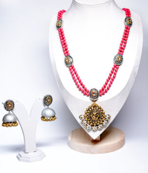 A pink beaded double-strand necklace with an antique gold temple-style kundan pendant, paired with matching silver-and-gold jhumka earrings, displayed on a white jewellery bust.