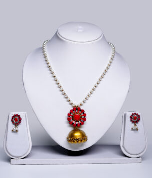 Pearl beaded necklace with a coral-pink floral pendant and gold jhumka drop, paired with matching stud earrings, displayed on a white jewellery bust.