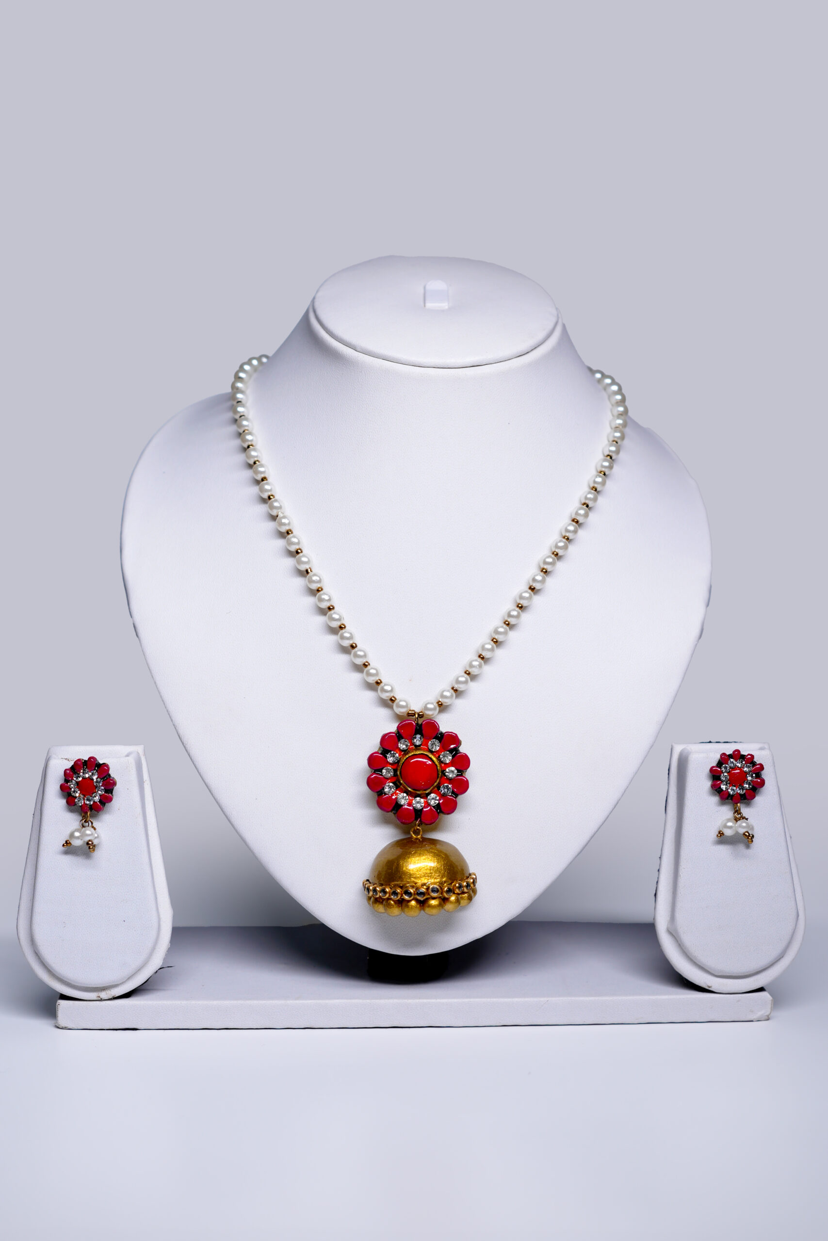 Pearl beaded necklace with a coral-pink floral pendant and gold jhumka drop, paired with matching stud earrings, displayed on a white jewellery bust.
