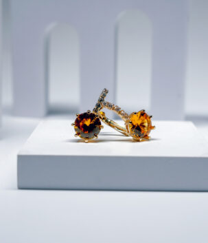 citrine solitaire stud earrings with a crystal-lined bar, featuring a warm amber stone, displayed on a white pedestal.