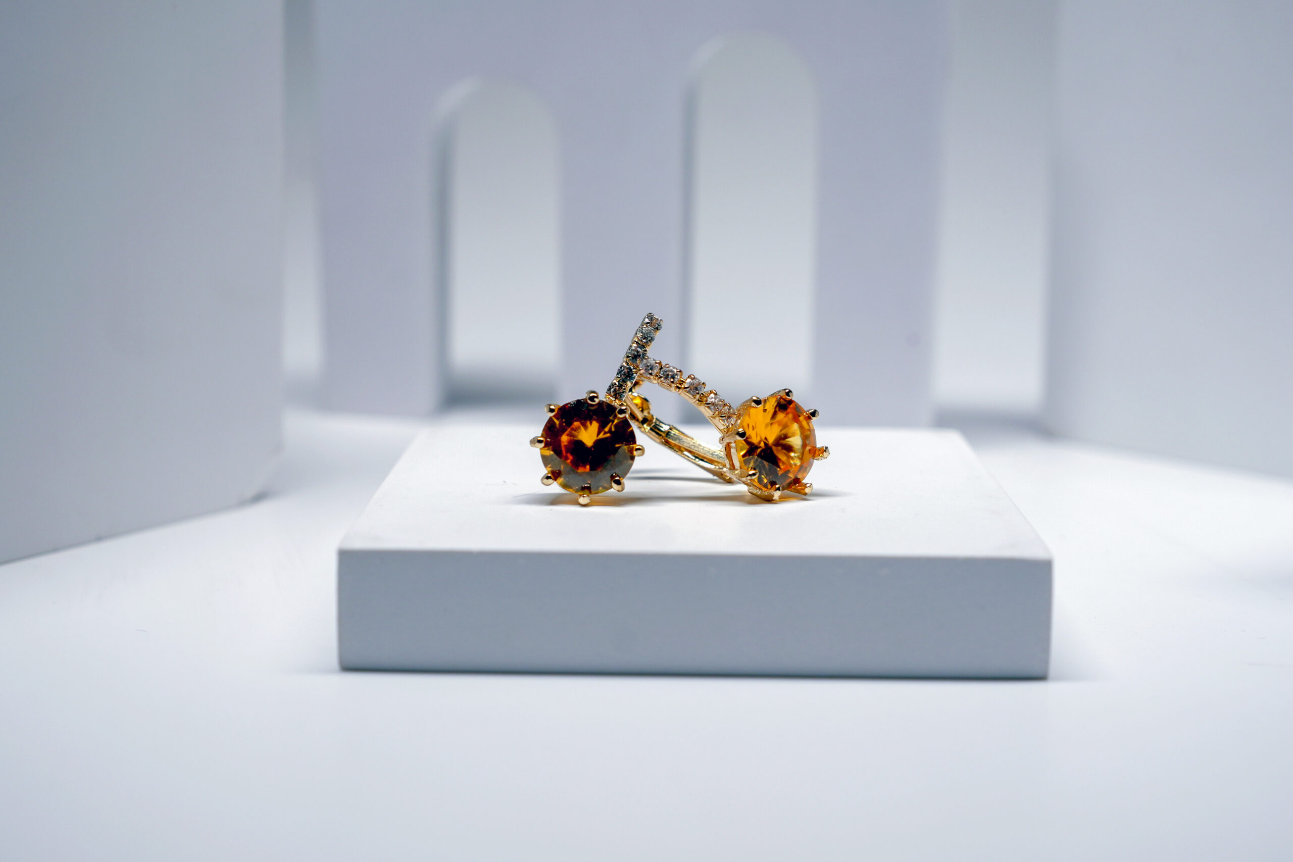 citrine solitaire stud earrings with a crystal-lined bar, featuring a warm amber stone, displayed on a white pedestal.