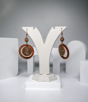 Wooden rose drop earrings with a carved rose medallion inside a copper-tone circle frame, displayed on a jewellery stand.