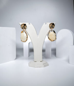 Gold plated drop earrings featuring a cream marble-effect resin stone in an organic hammered frame, displayed on a jewellery stand.