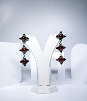 Oxidised silver tiered drop earrings featuring three red cabochon stones in an ornate vintage-style frame, displayed on a jewellery stand.