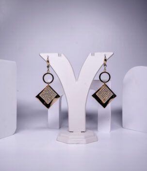 Black enamel drop earrings featuring a crystal-studded diamond shape and circular link, displayed on a jewellery stand.