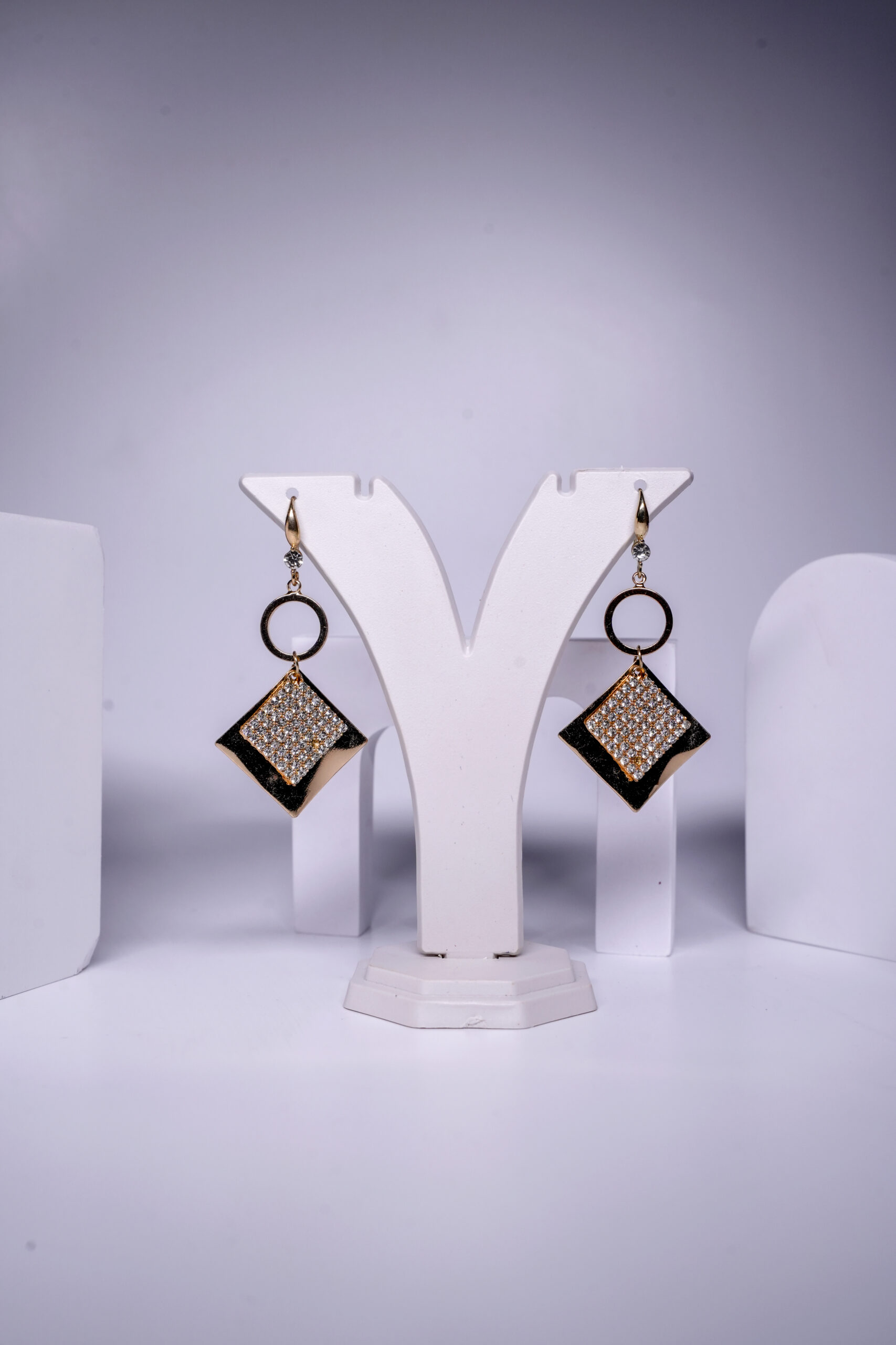 Black enamel drop earrings featuring a crystal-studded diamond shape and circular link, displayed on a jewellery stand.