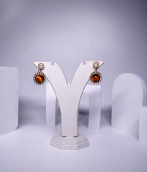 Gold plated pearl and amber stone drop earrings featuring a sparkling crystal halo, displayed on a jewellery stand.
